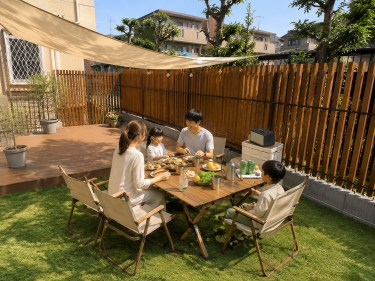 木製目隠しフェンス（メッシュフェンス用）を設置した庭で、周囲の視線を気にせず家族が食事を楽しむウッドデッキとガーデンスペースの施工事例