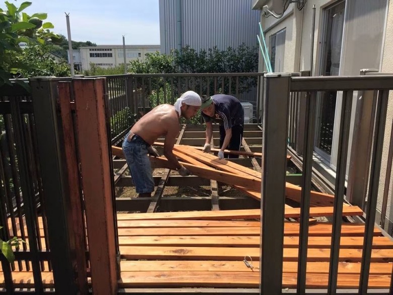 既存のウッドデッキ下地に新しいサイプレスの床板を二人で並べて張り替えているDIY施工風景