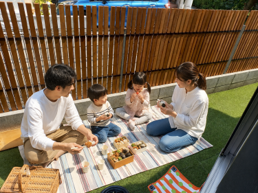 木製目隠しフェンス（メッシュフェンス用）を設置した庭で、周囲の視線を気にせず家族がお弁当を囲んでピクニックを楽しむ施工事例
